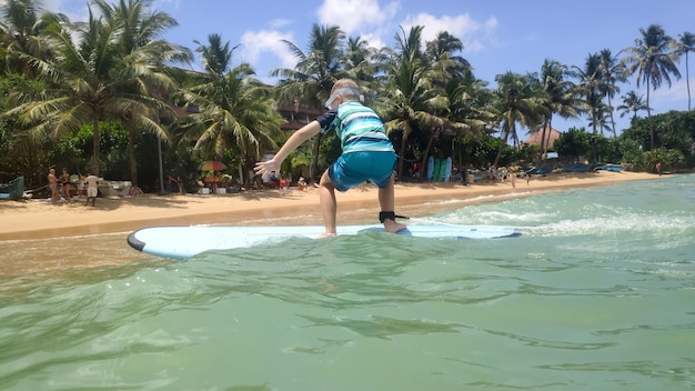 The boy is surfing on the waves in the blue sea Sandy beach with beautiful palm treesxA