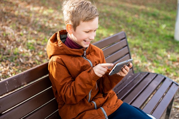 The boy is talking by video on the phone sitting on a bench and laughing