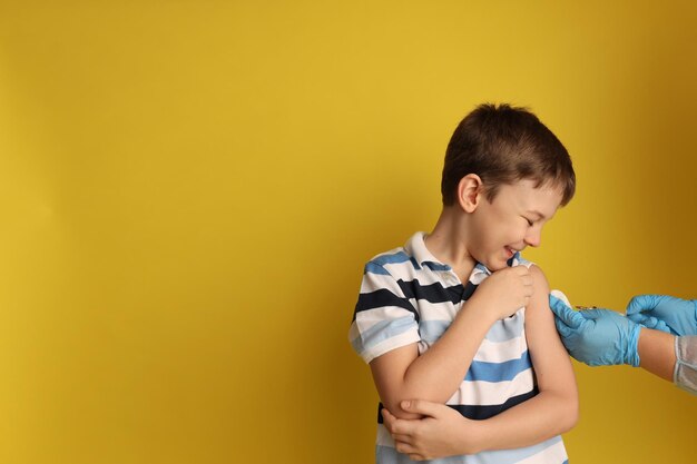 The boy is vaccinated Against the background of a hand in gloves and with a syringe Space for text