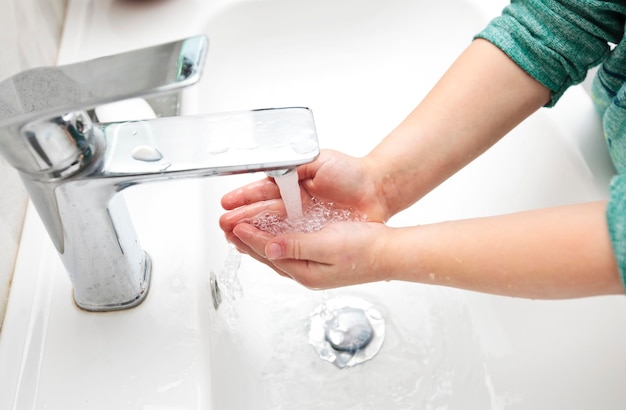 The boy is washing his hands with soap under the water