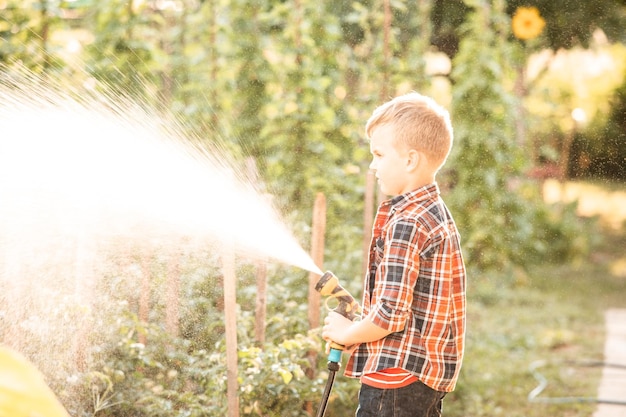 The boy is watering the garden bed using a hose