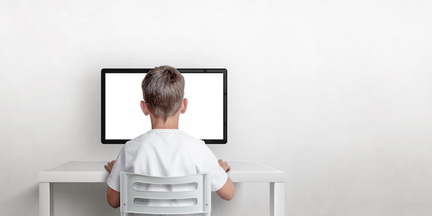 Boy is working on the computer his back is turned Isolated computer display for mockup Copy space on the wall The concept of working and learning on the computer