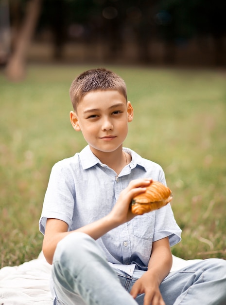 Boy kid sitting on picnic summer vacation and eating freshly baked croissant sandwich.