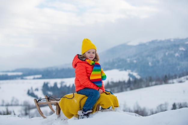 Boy kid sliding with sledge in the winter snow christmas kids holidays and happy new year