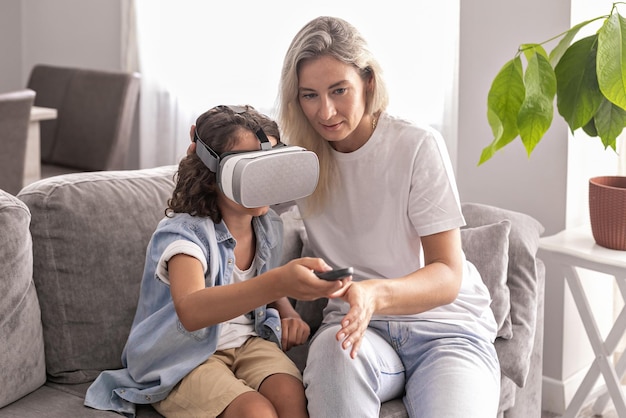 Boy kid wearing virtual reality headset with his mother vr glasses in living room at home having fun