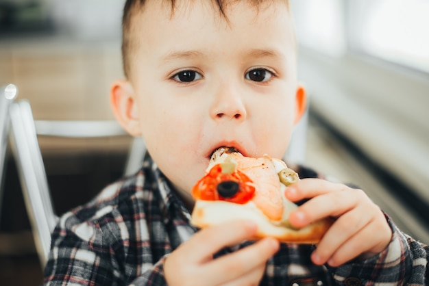 The boy in the kitchen at home eating pizza with salmon