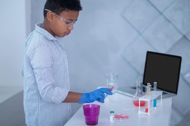 A boy in a lab coat working with test tubes and looking involved