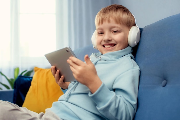 The boy lies on the couch and watches games on the tablet