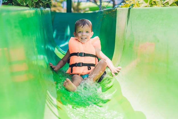 A boy in a life jacket slides down from a slide in a water park.