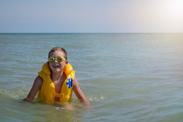 boy in a life jacket in the water. joyful child spends summer vacation at the sea on a sunny day. banner