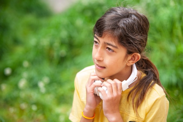 Boy listening to music with white headphones outside next to a green meadow