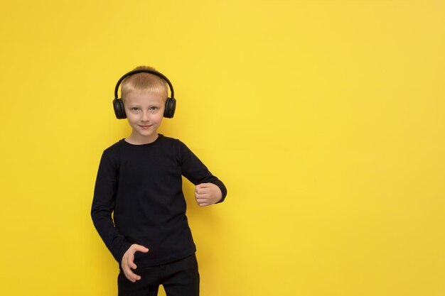 Boy listens to music with headphones and dances on a yellow background with copy space