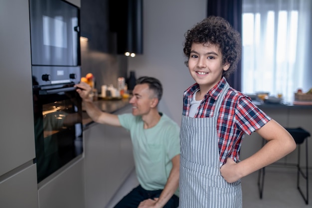 Boy looking at camera and man behind near oven