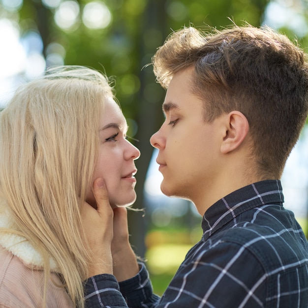 The boy looks tenderly at girl, hands clasped her face and wants to kiss