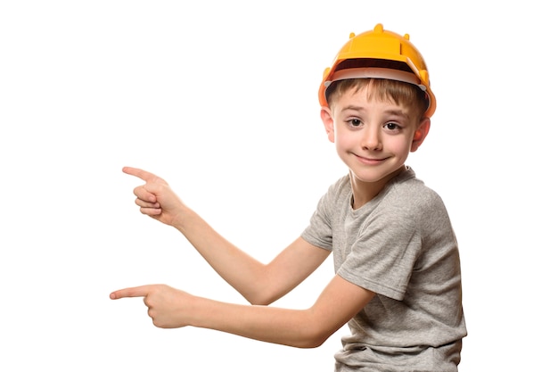 Boy in orange construction helmet shows forefingers aside. Portrait. Isolate on white wall.