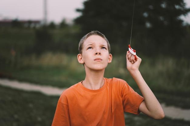 A boy in an orange shirt looks up at a kite