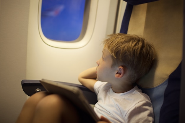 Boy in plane looking out illuminator with pad on lap