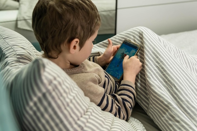 Boy playing game on smartphone comfortably sitting on the bed