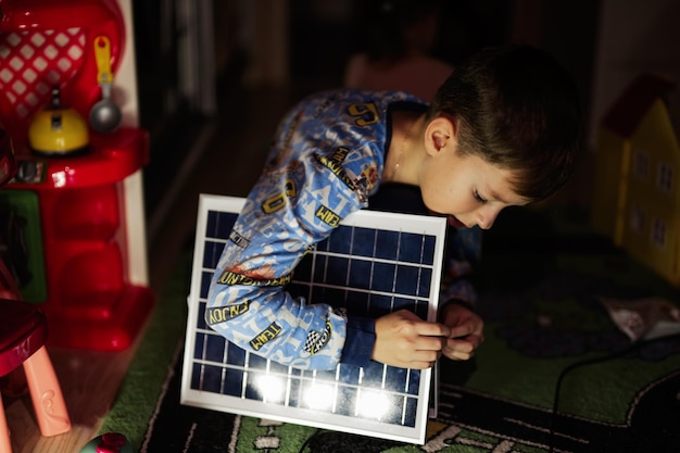 Boy playing at home during a blackout using alternative lighting with solar panel