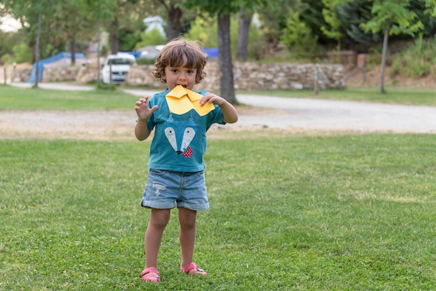 Boy playing toss paper plane outdoors looking away Portrait of a cheerful caucasian boy playing in the spring and summer park having fun on the weekend