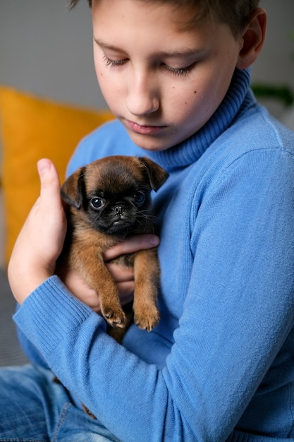 Boy playing with baby dog. Kid play with puppy at home. Little boy and griffon or brabanson dog