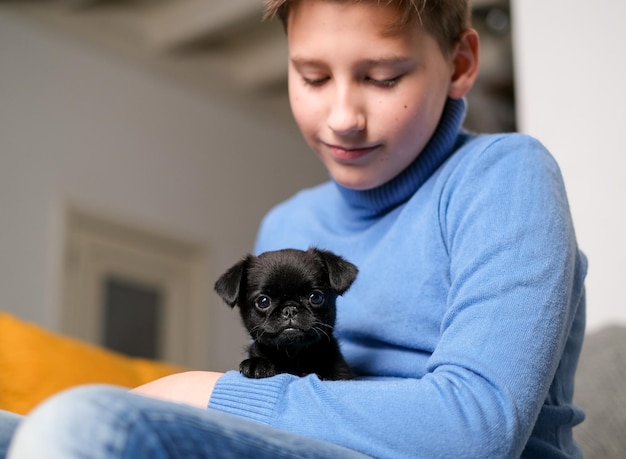 Boy playing with baby dog. Kid play with puppy at home. Little boy and griffon or brabanson dog