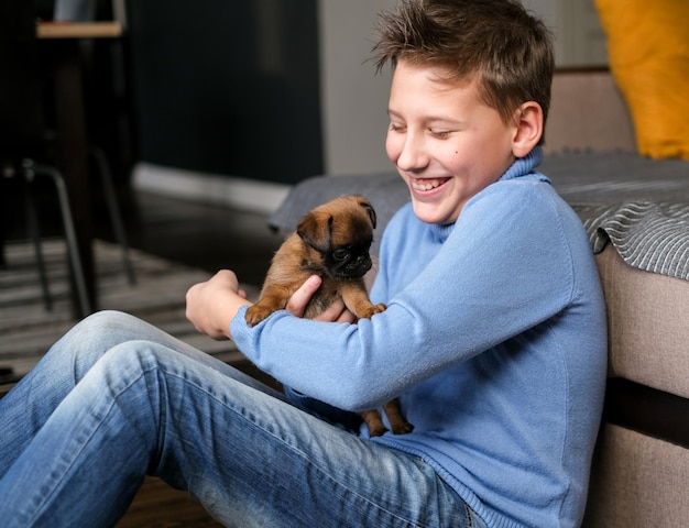 Boy playing with baby dog. Kid play with puppy at home. Little boy and griffon or brabanson dog