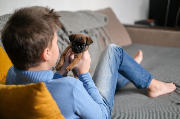 Boy playing with baby dog. Kid play with puppy at home. Little boy and griffon or brabanson dog