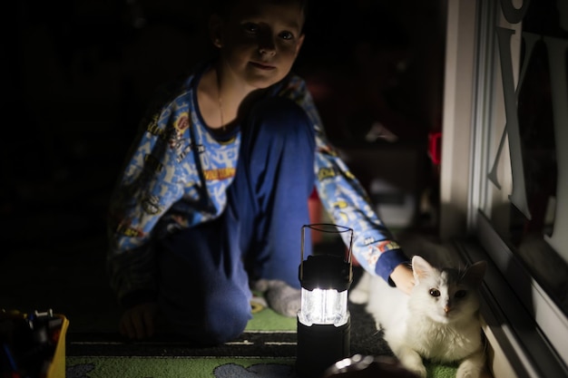 Boy playing with cat at home during a blackout using led lantern