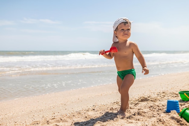 Boy playing with toys on the beach building beads and turrets smiling at someone behind the scenes on summer vacation