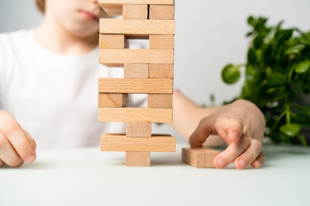 A boy plays a board game builds a tower of wooden cubes hands closeup a logical game of jenga for