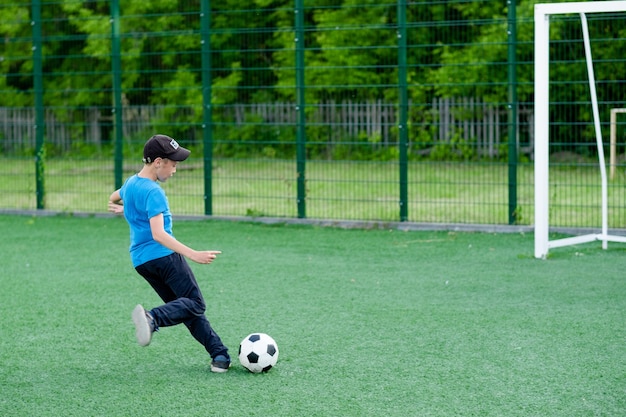 The boy plays football in the yard on the lawn Child kicks the ball