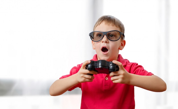 The boy plays games with a joypad and 3d glasses. His mouth slightly open with excitement.