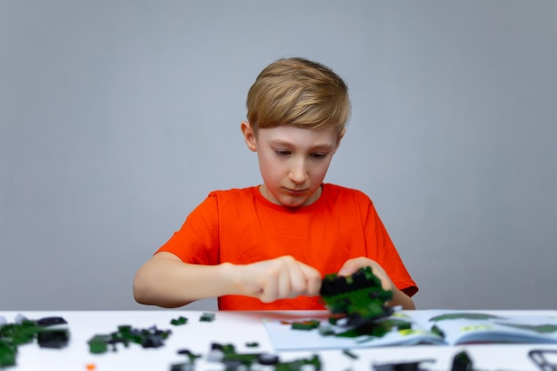 A boy plays with a plastic constructor focused on the process of assembling parts