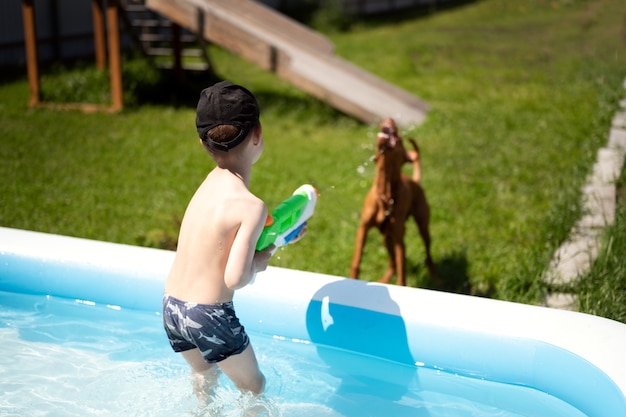 A boy in the pool is playing with a water pistol Shoots a jet of water at the dog the dog catches