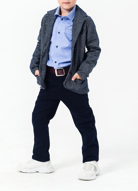 The boy poses in a school uniform on a white background The model is wearing a shirt jacket pants and sneakers Vertical photo