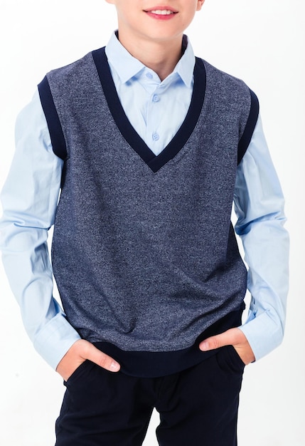 The boy poses in a school uniform on a white background The teenager is wearing a shirt vest and trousers Vertical photo