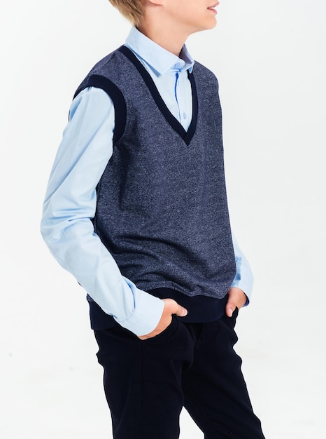 The boy poses in a school uniform on a white background The teenager is wearing a shirt vest and trousers Vertical photo