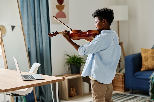 Boy practicing to play violin during online lesson