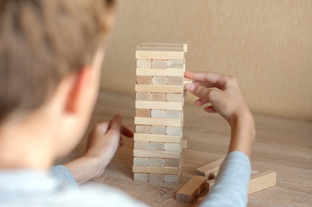 Boy pulls a block out of a wooden tower