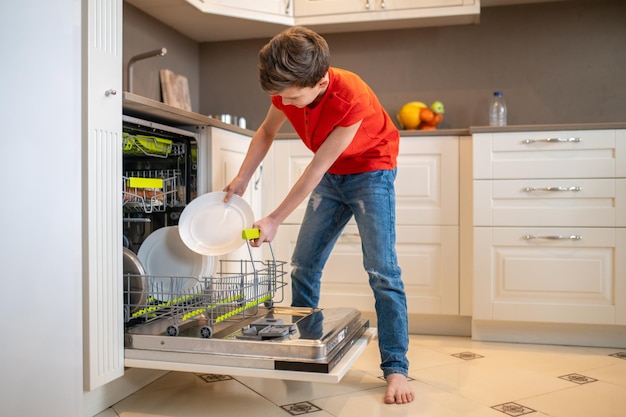 Boy putting dishes into an open dishwashing machine