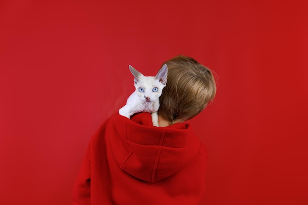 A boy in a red suit stands with his back and a small cat sits in his hood