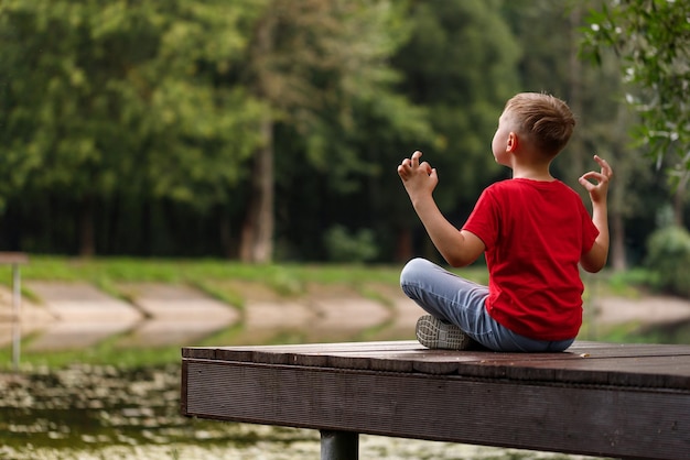 Boy in a red Tshirt meditates in the park A child in a yoga pose by the river