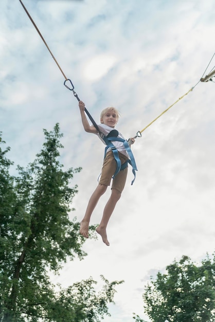 Boy rides trampoline in an amusement park and jumps high into sky Child has fun in the theme park