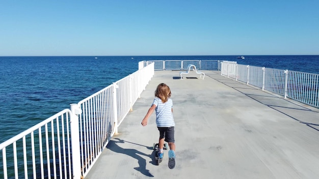 Boy riding scooter on a pier at sunyday