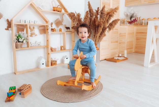 A boy riding a wooden rocking horse toy in a white bedroom with decor A child is playing in the nursery Toys for kids children's interior