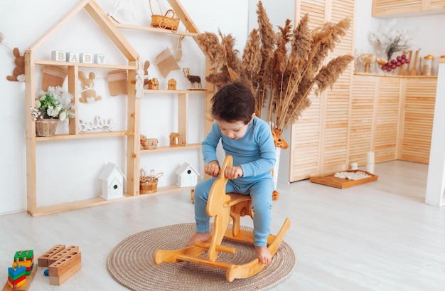 A boy riding a wooden rocking horse toy in a white bedroom with decor A child is playing in the nursery Toys for kids children's interior