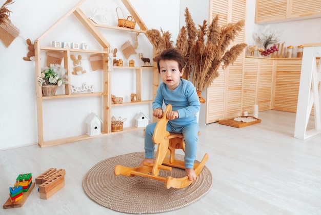 A boy riding a wooden rocking horse toy in a white bedroom with decor A child is playing in the nursery Toys for kids children's interior