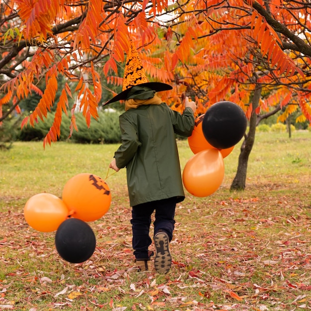 A boy running in the autumn park with a Halloween pumpkin balloons