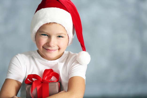 Boy in Santa hat with gift box on grey background